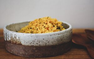 Image of a ceramic dish filled with spiced yellow rice. Recipe by Lunch Lady Lou