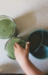 A toddlers hand going in a bowl of green smoothie. Simple healthy Green smoothie recipe by Lunch Lady Lou