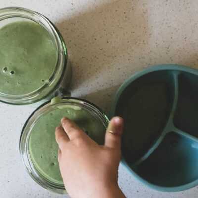 A toddlers hand going in a bowl of green smoothie. Simple healthy Green smoothie recipe by Lunch Lady Lou