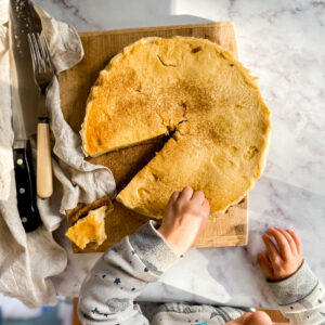 Image of easy homemade custard tart with toddler sitting in front of it, taking a slice. Recipe by Lunch Lady Lou